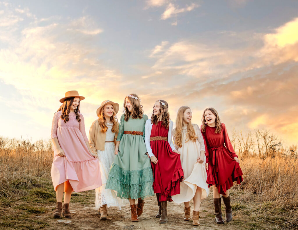 6 girls walking on a dirt path through Cliff Cave Park wearing fancy beautiful dresses, laughing, and having a good time.