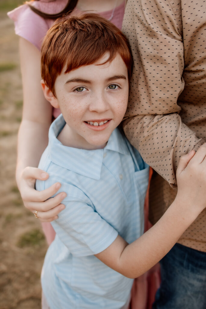 a close up of a little boy with red hair holding on to his dad's arm.