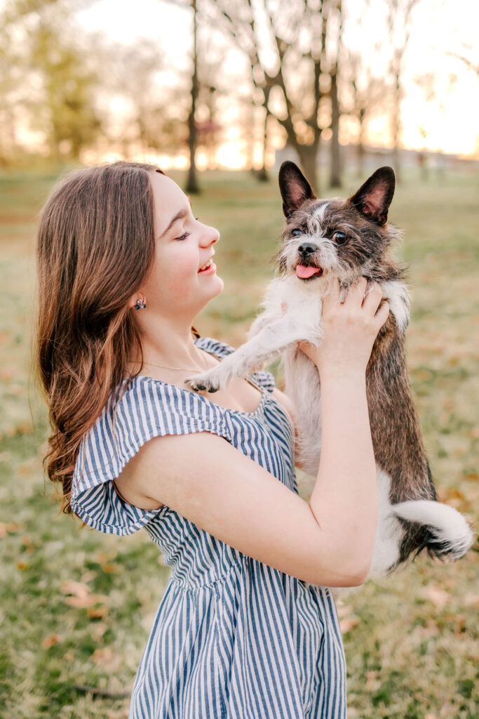 A baeutiful young girl holding her dog in the park at sunset.