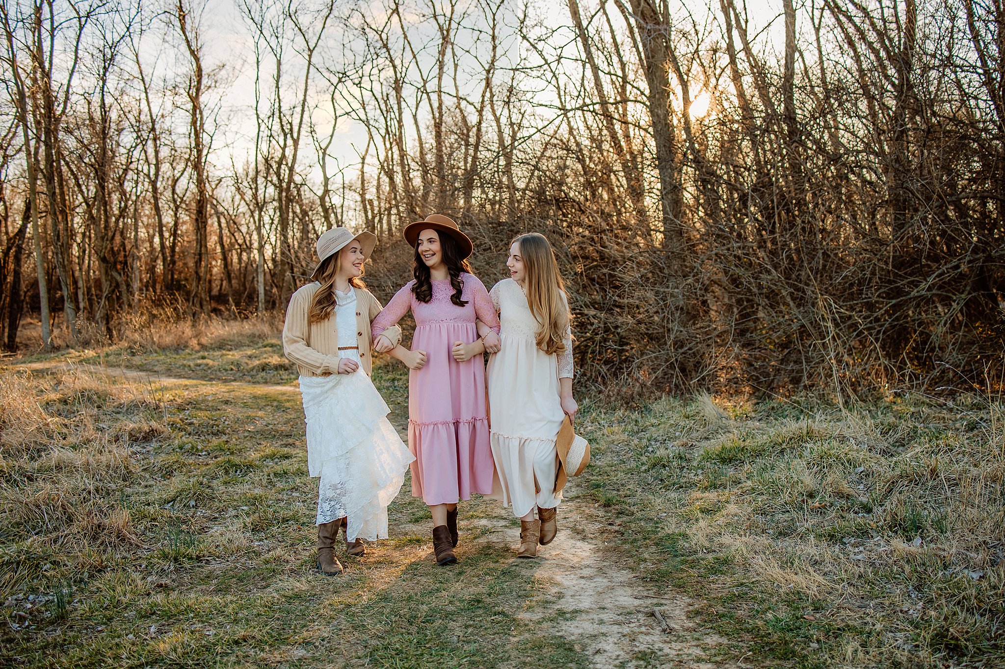 Three young girls with long flowing hair walk down a dirt path in long dresses hair salons in saint louis