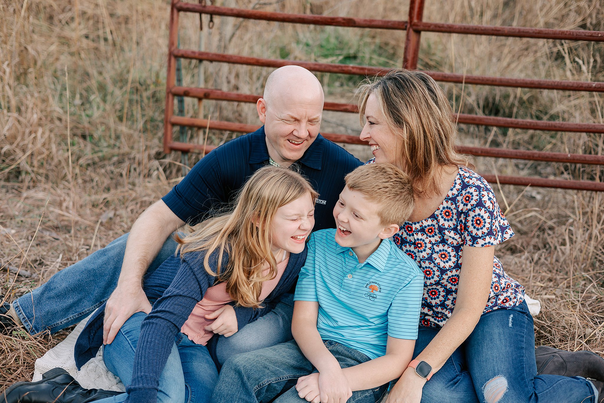 A family of four sits in the grass of a field in front of a rusty farm gate things to do in oakville