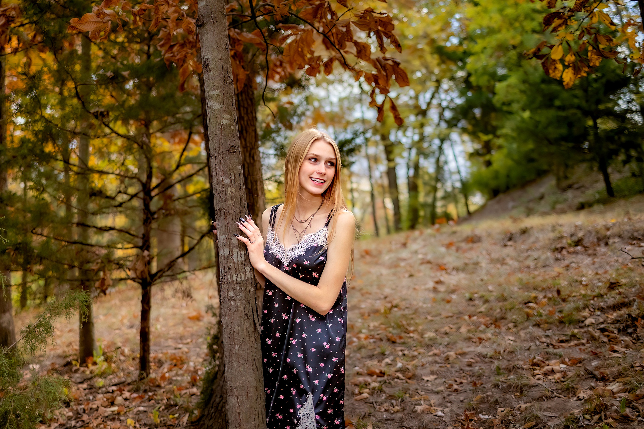 A high school senior in a black and pink dress leans against a tree in fall in the woods act prep st louis