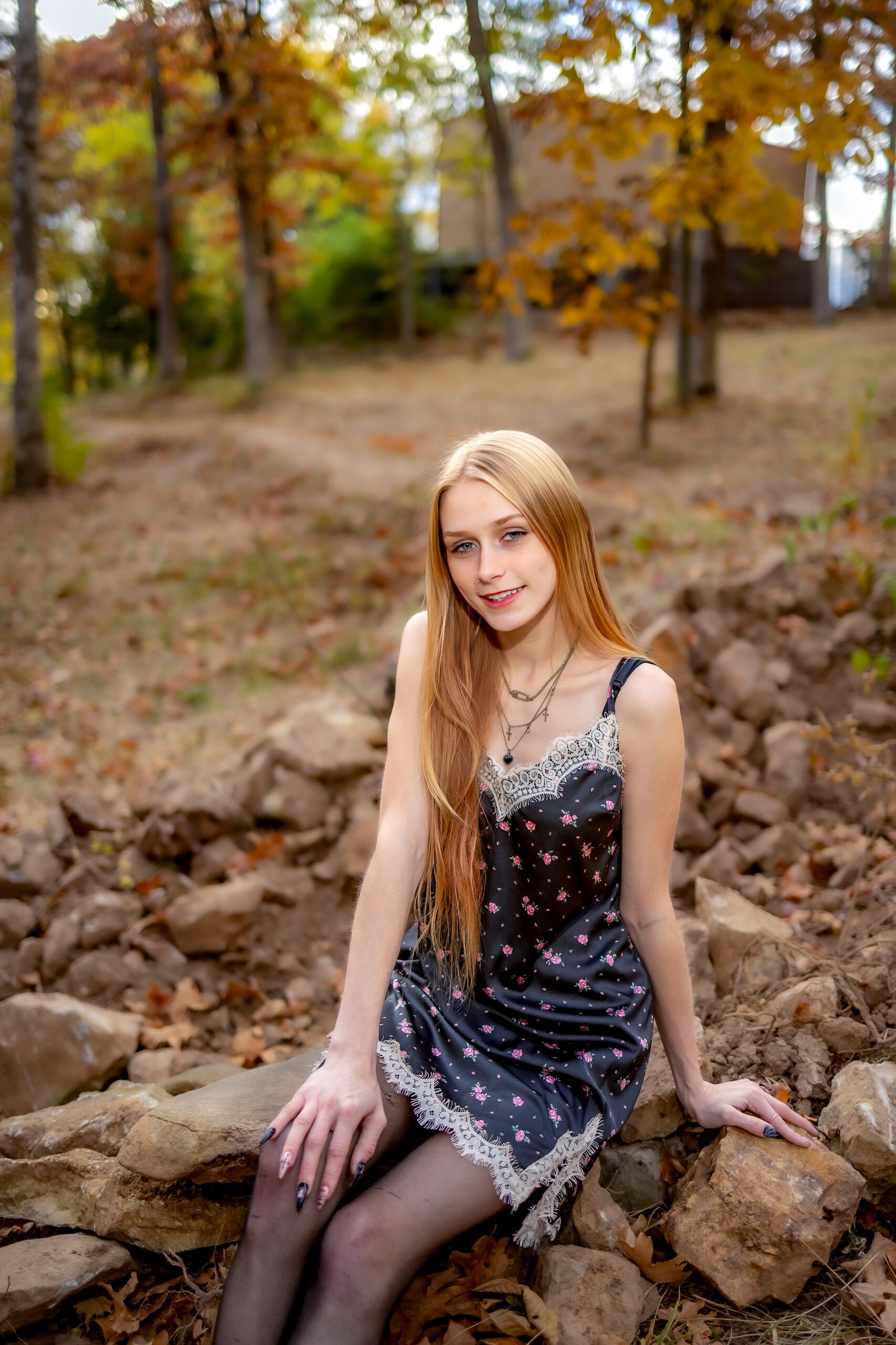 A high school senior in a black and pink dress sits on a rock wall in fall act prep st louis