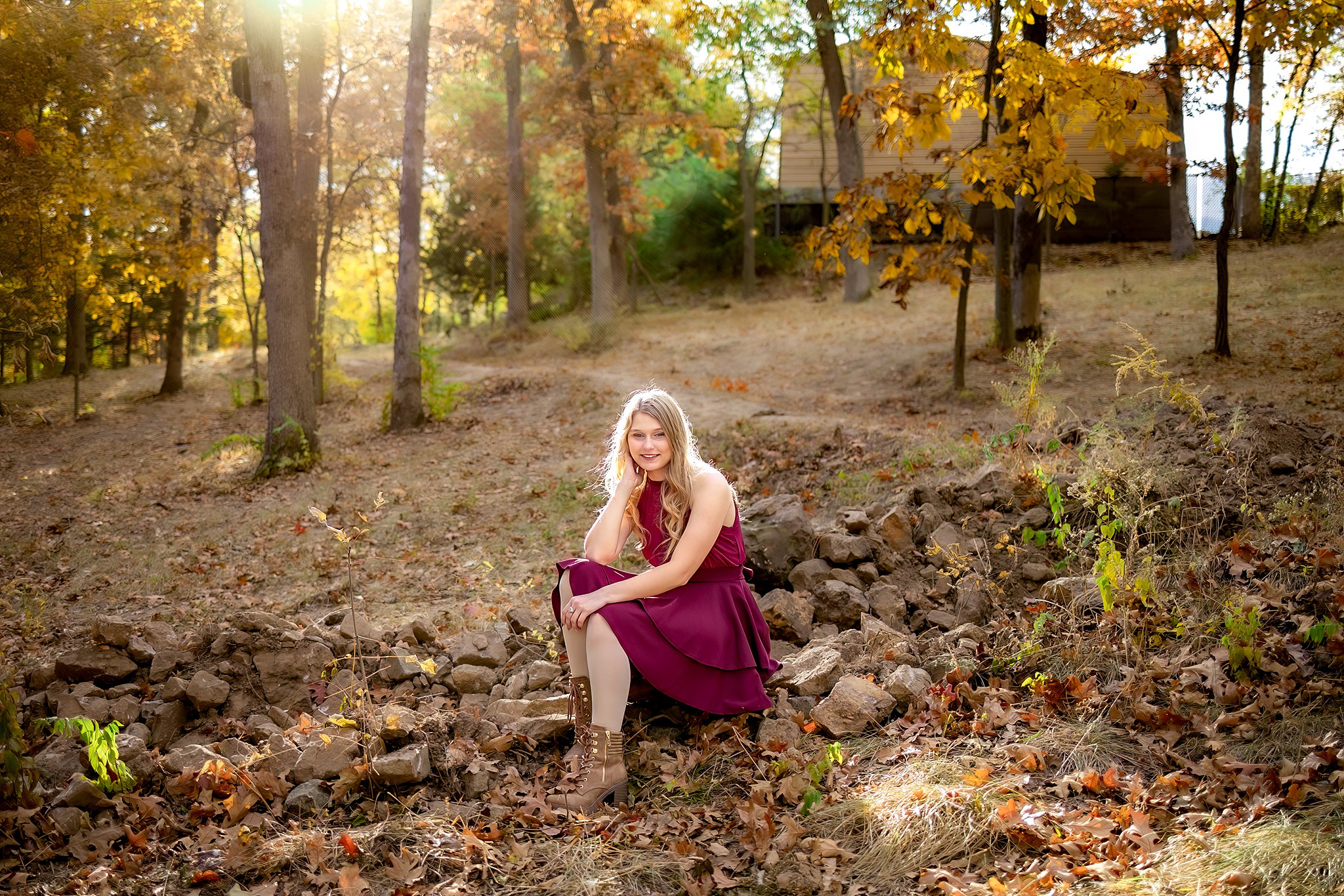 A high school senior in a purple dress and brown boots sits on some rocks in fall in a yard boutiques in St Louis