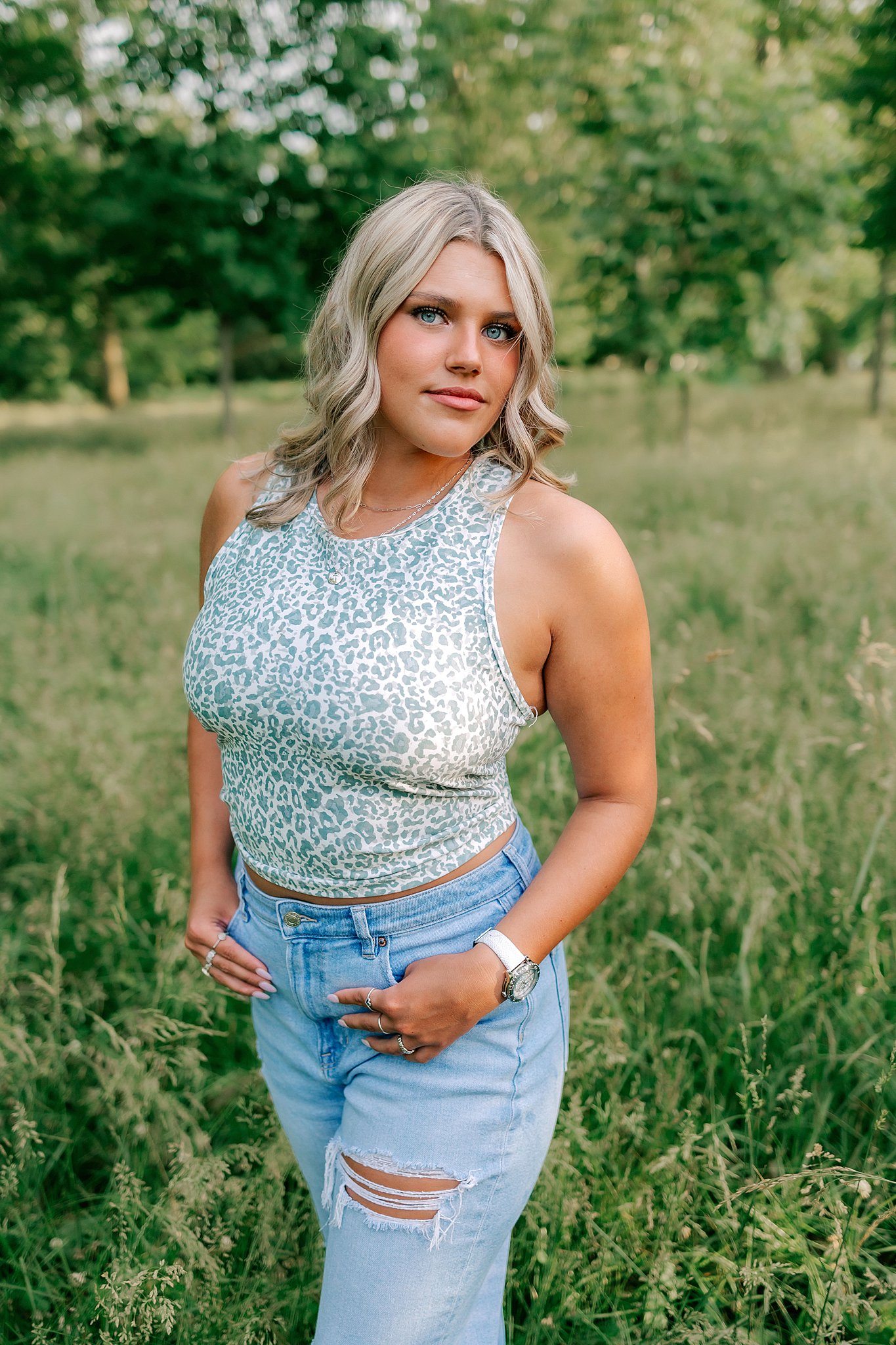 A high school senior stands in tall green grass with thumbs in her jean pockets st louis colleges