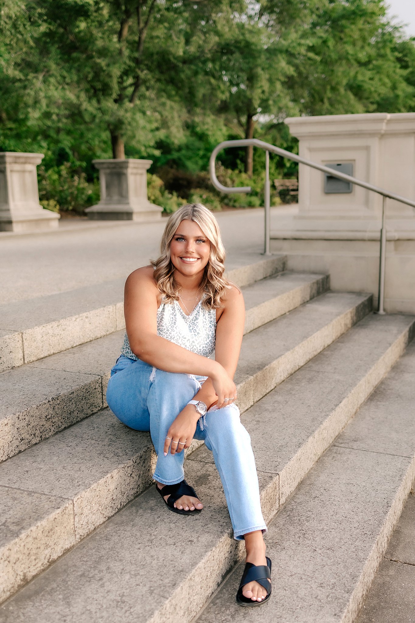 A high school senior sits on concrete steps in jeans and a white blouse st louis colleges