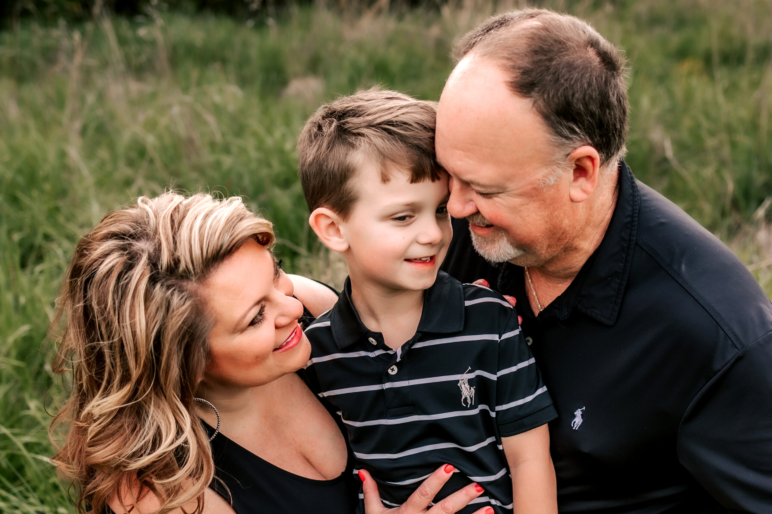 A young boy sits on the lap of his father and mother in a grassy field st louis pediatricians