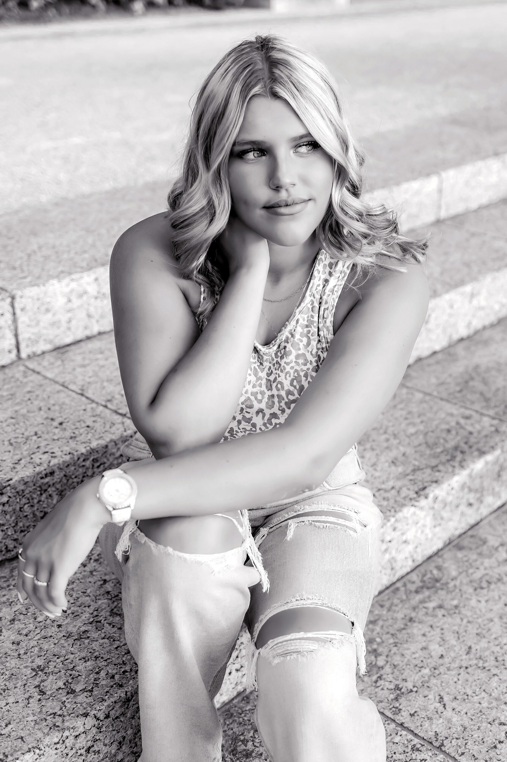 A high school senior sits on marble steps in ripped jeans and a leopard top st louis prom dresses