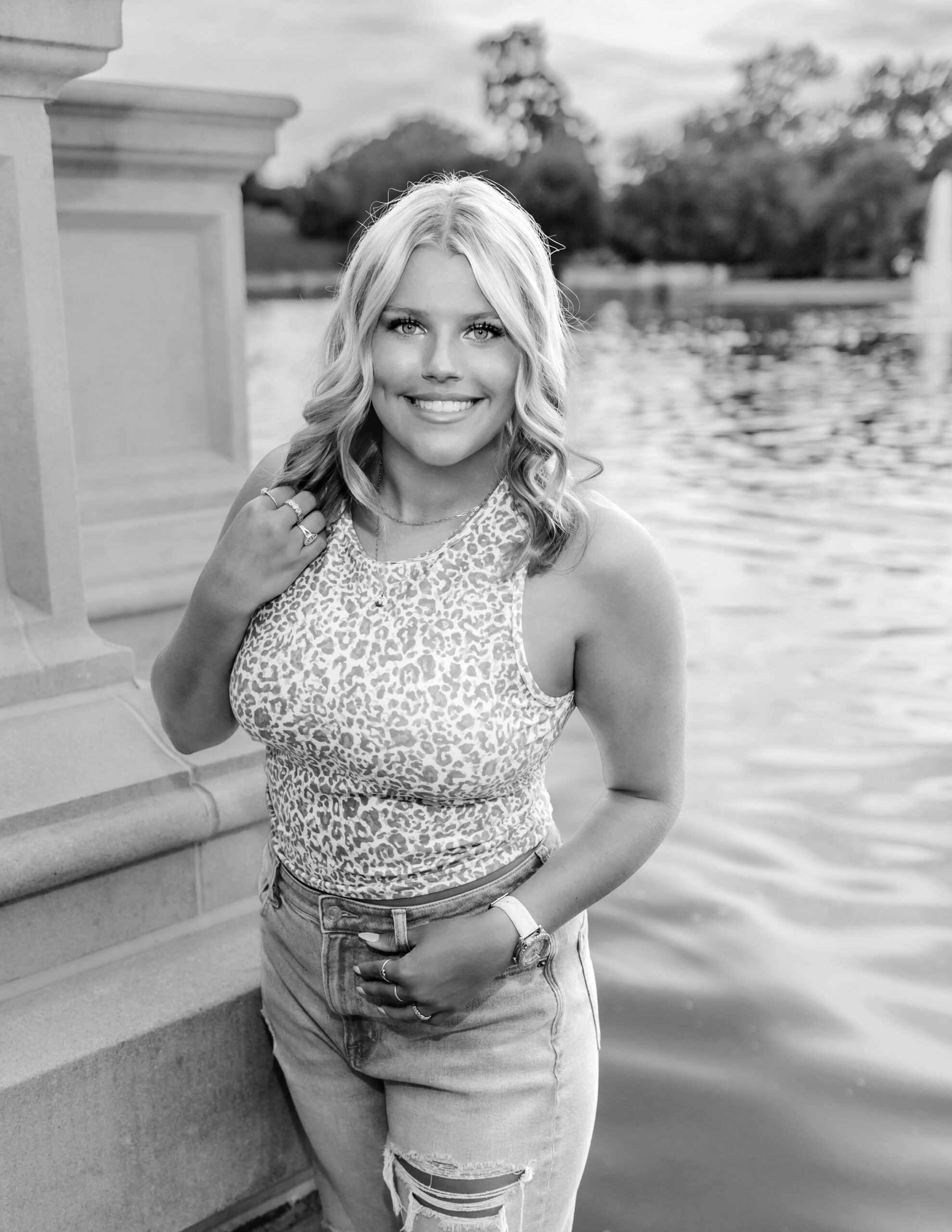 A high school senior stands on the edge of a lake in a leopard top and jeans st louis prom dresses