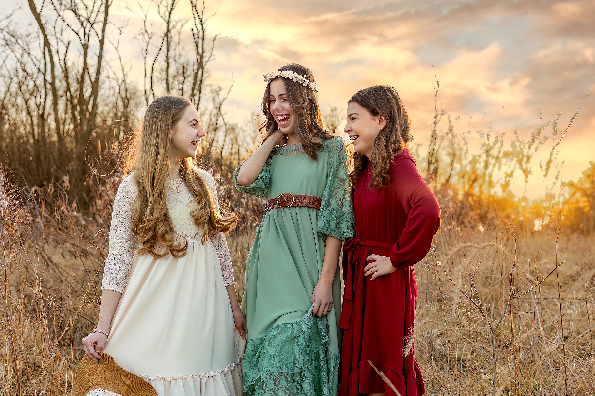 Three sisters in long dresses laugh together in a field of golden grass at sunset things to do in st louis with kids