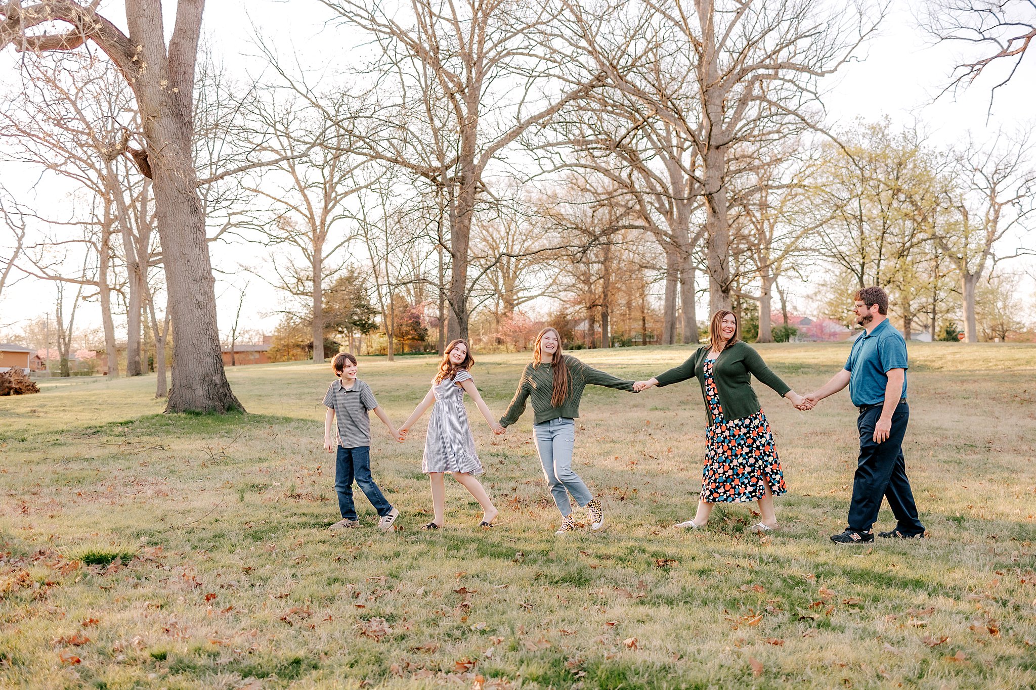 A family of five walk through a park field holding hands