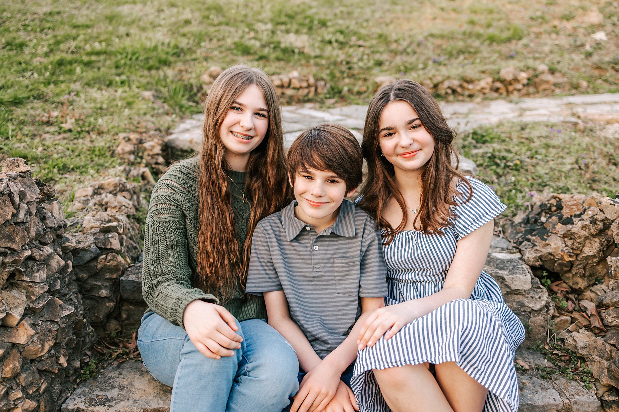 Three siblings sit on stone steps in a park best parks in St-Louis