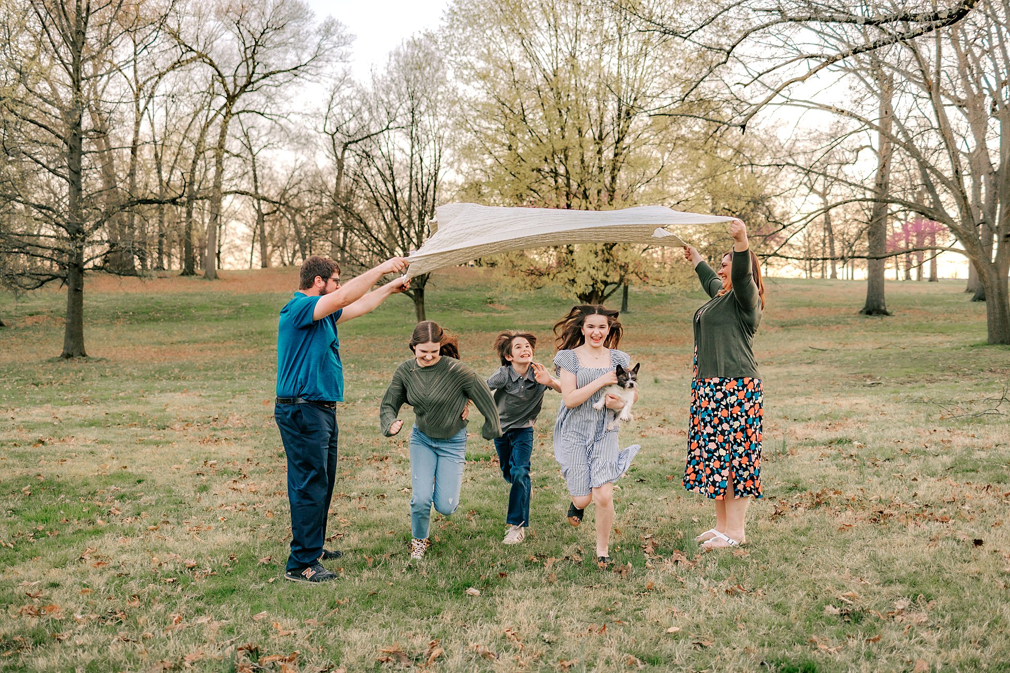 A mother and father raise a sheet while their three children and dog run underneath it between them best parks in St-Louis