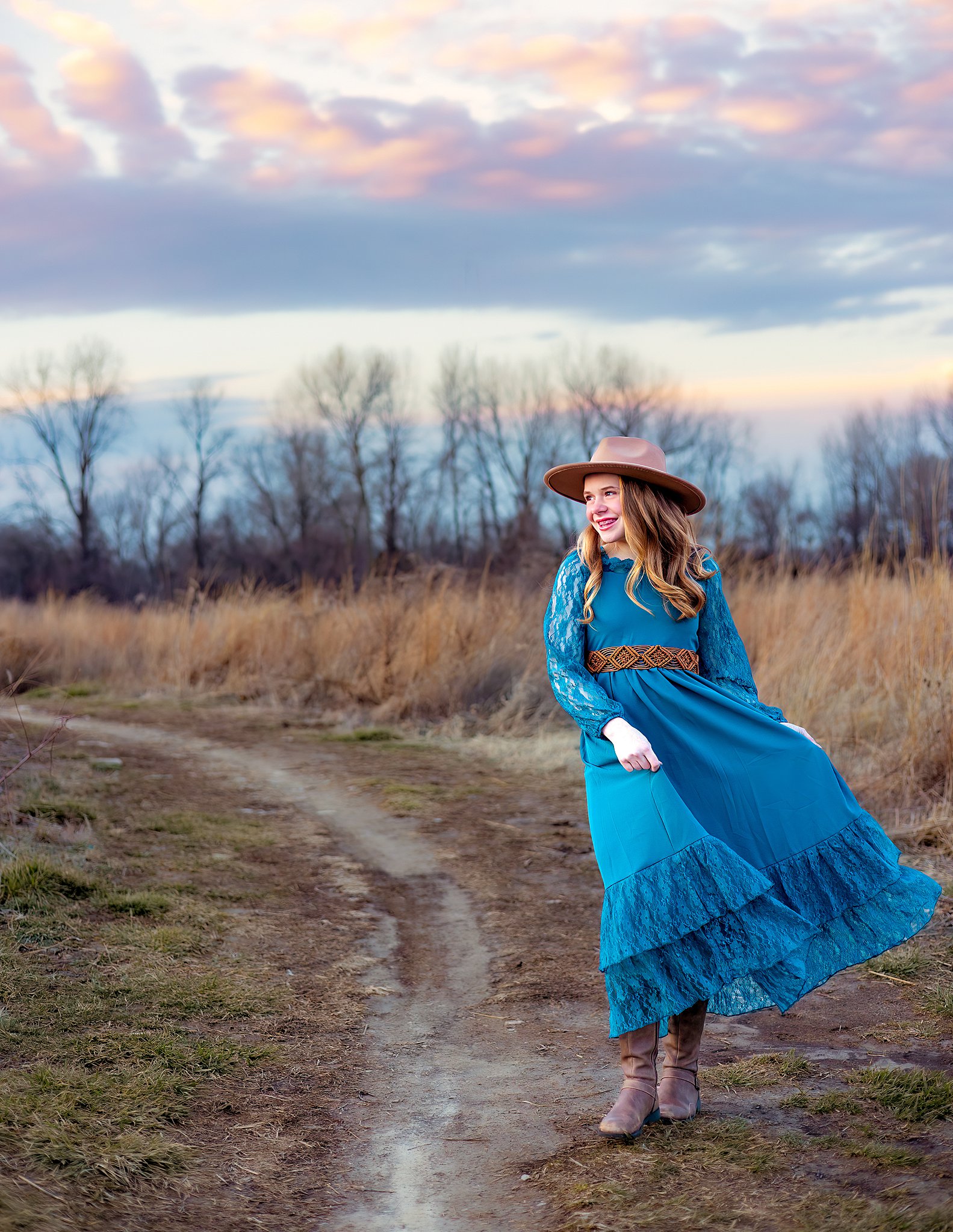 A high school senior plays with her dress in a trail surrounded by tall grass