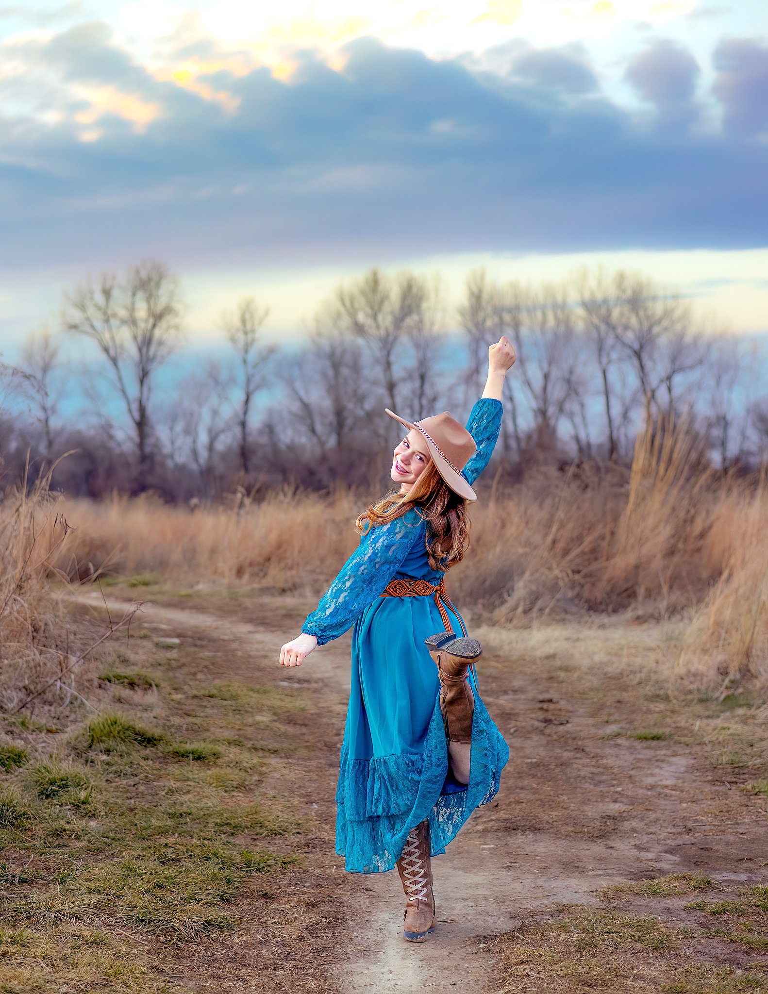 A high school senior in boots and a blue dress dances in a park trail st louis dance studios