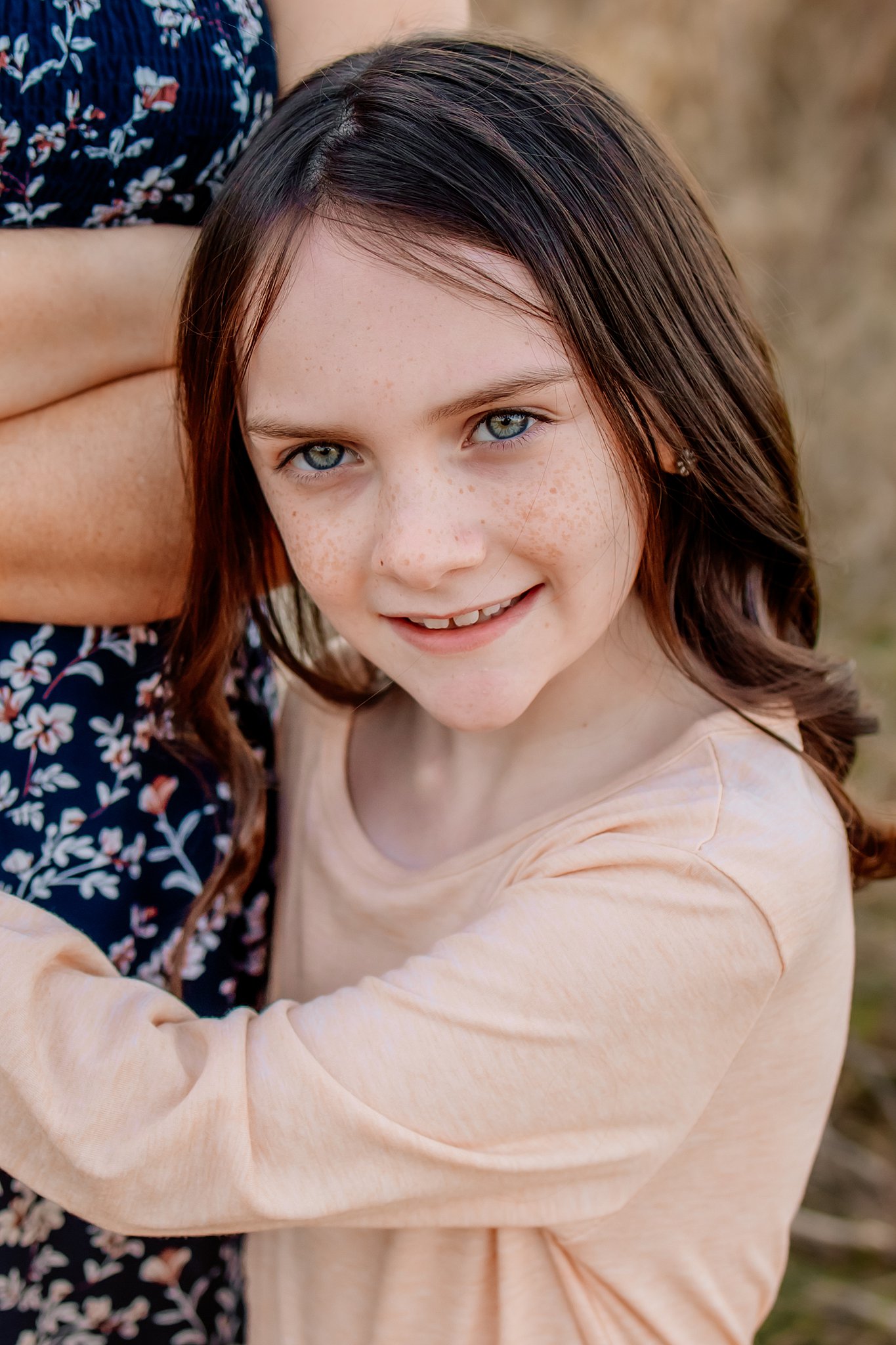 A young girl hugs onto her mom while standing in a park