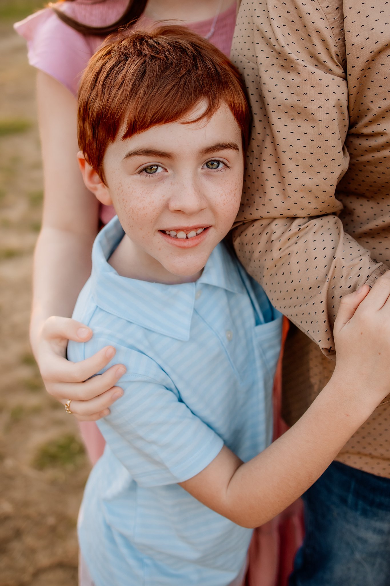 A young boy in a blue polo hugs on his father while standing in a park at sunset st louis pediatric dentist