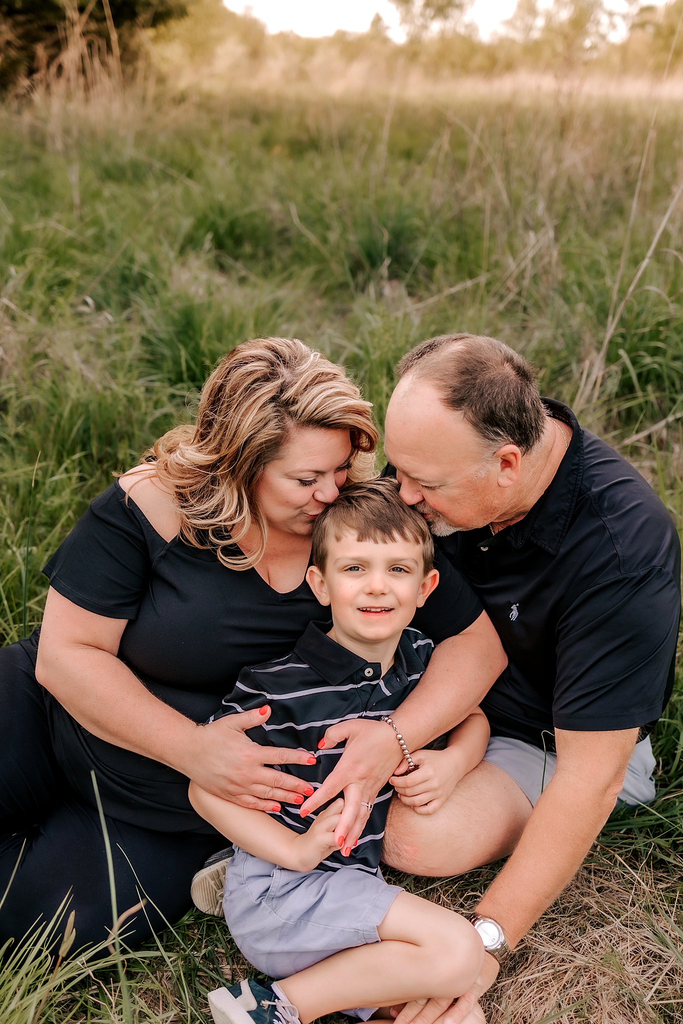 A mother and father sit on the ground with their son kissing his head between them st louis preschools