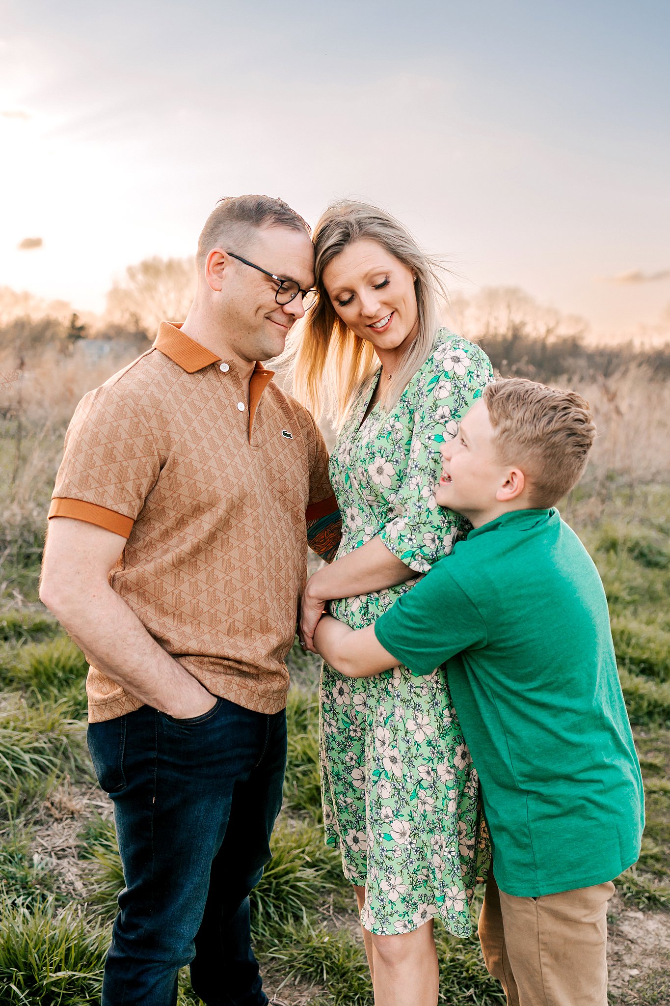 A young boy in a green polo hugs on his mother while dad hugs her as well