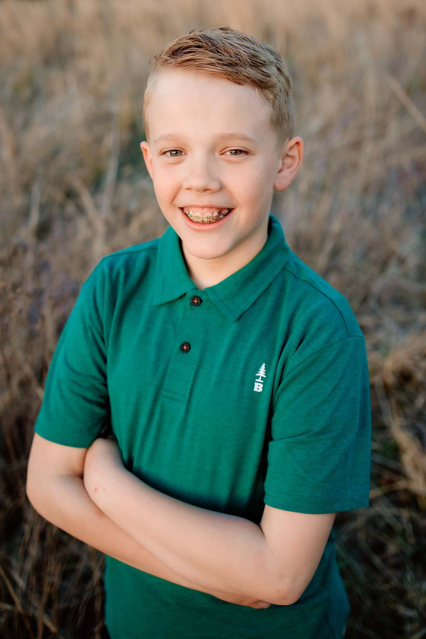 A young boy crosses his arms in a green polo while standing in tall grass st louis swim lessons