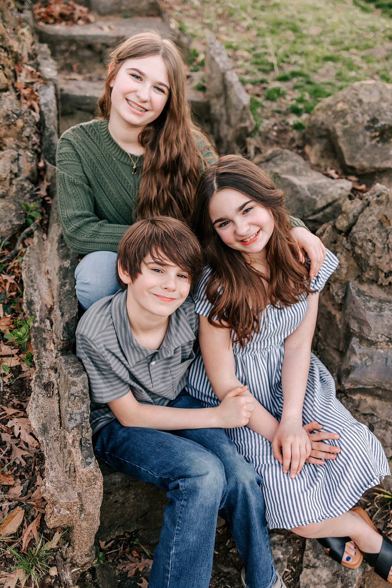 Three siblings sit together on stone stairs in a park st louis youth soccer clubs