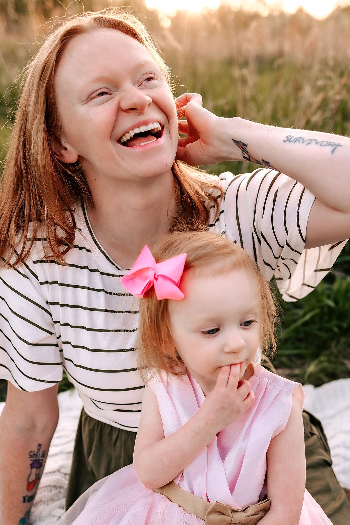 A mother sits on a picnic blanket in a field with her young daughter on her lap