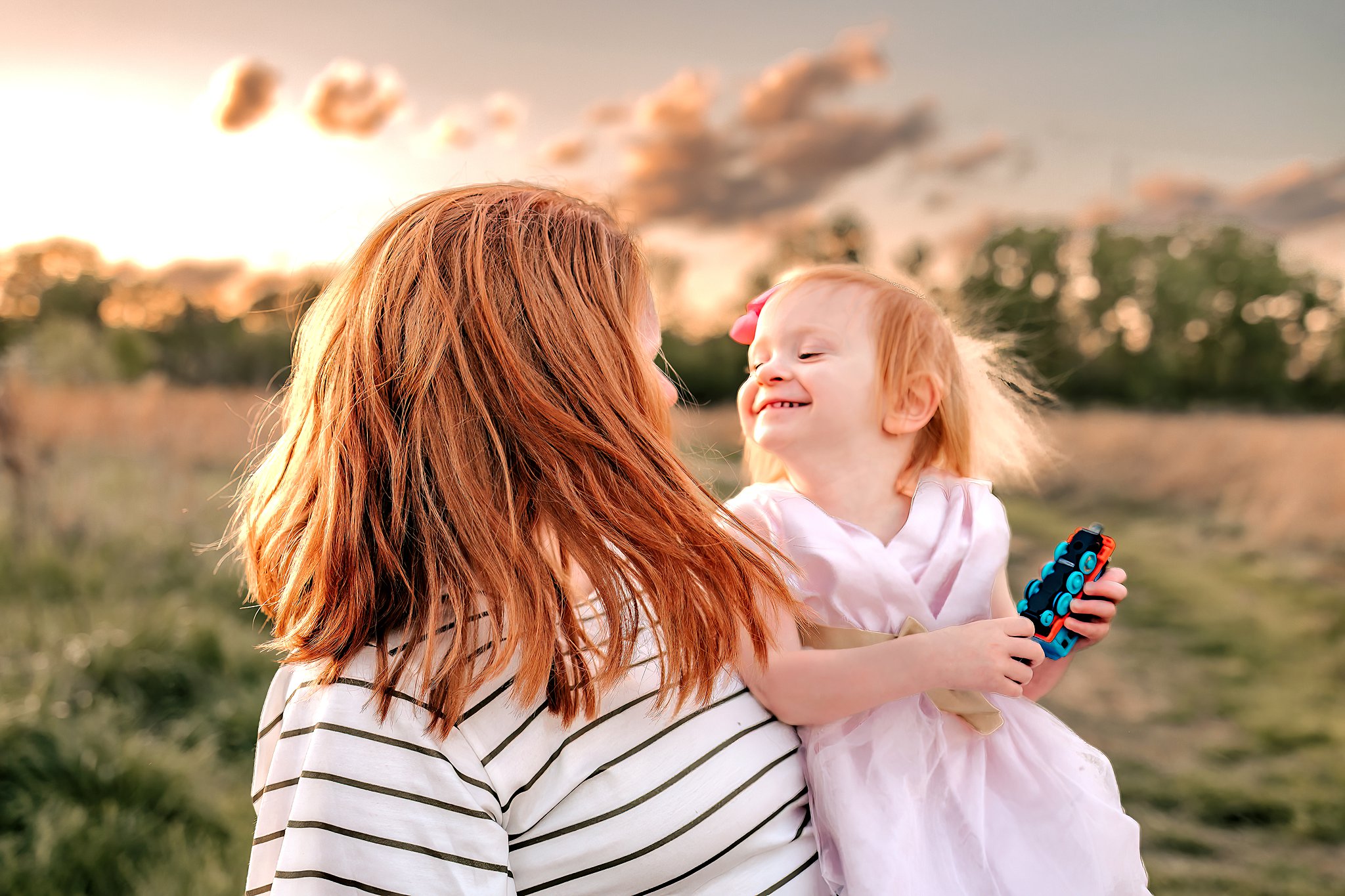 A mother plays with her daughter and a toy train in a field at sunset toy stores st louis