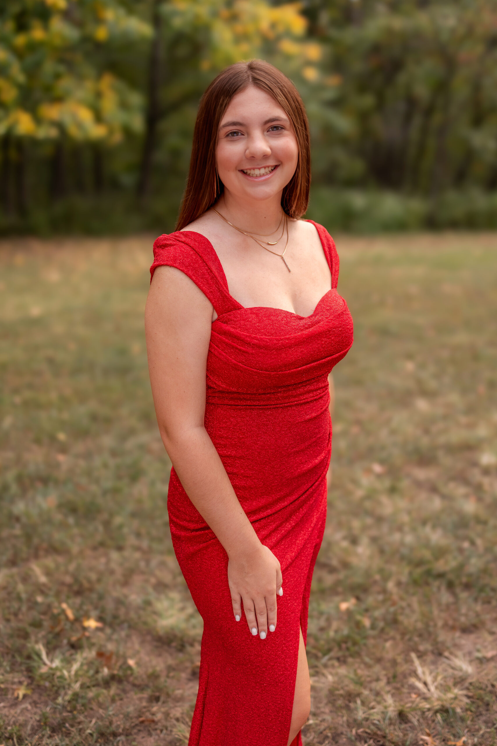 A young high school senior is dressed in a long red prom dress. She is posing for her Senior Prom Photos with Foppiano Photography.