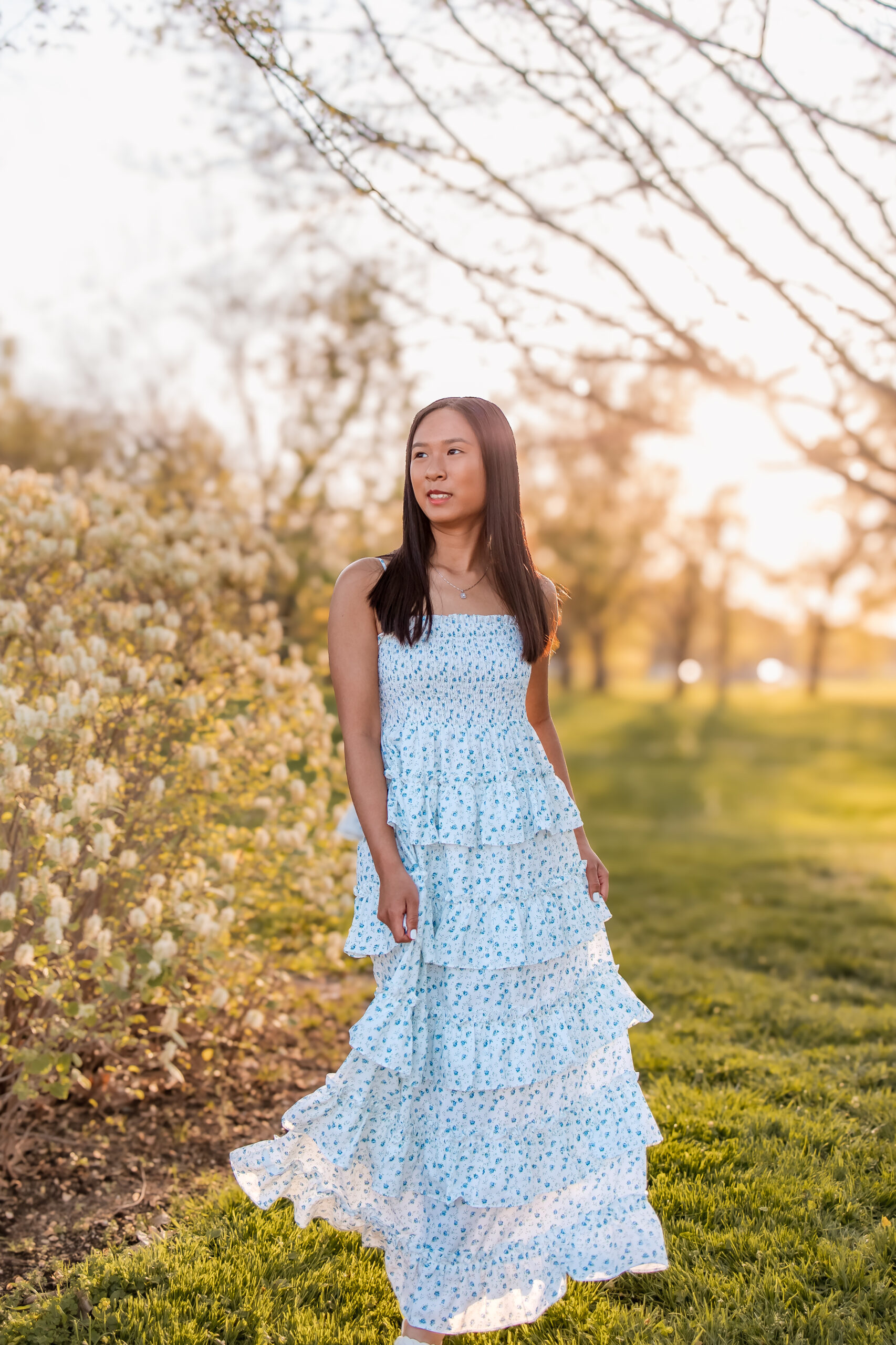 a lovely young lady is walking through the park at sunset, she is swishing her dress and looking up and to the right at sunset. She understood the assignment for what to wear to your senior photos in St. Louis.