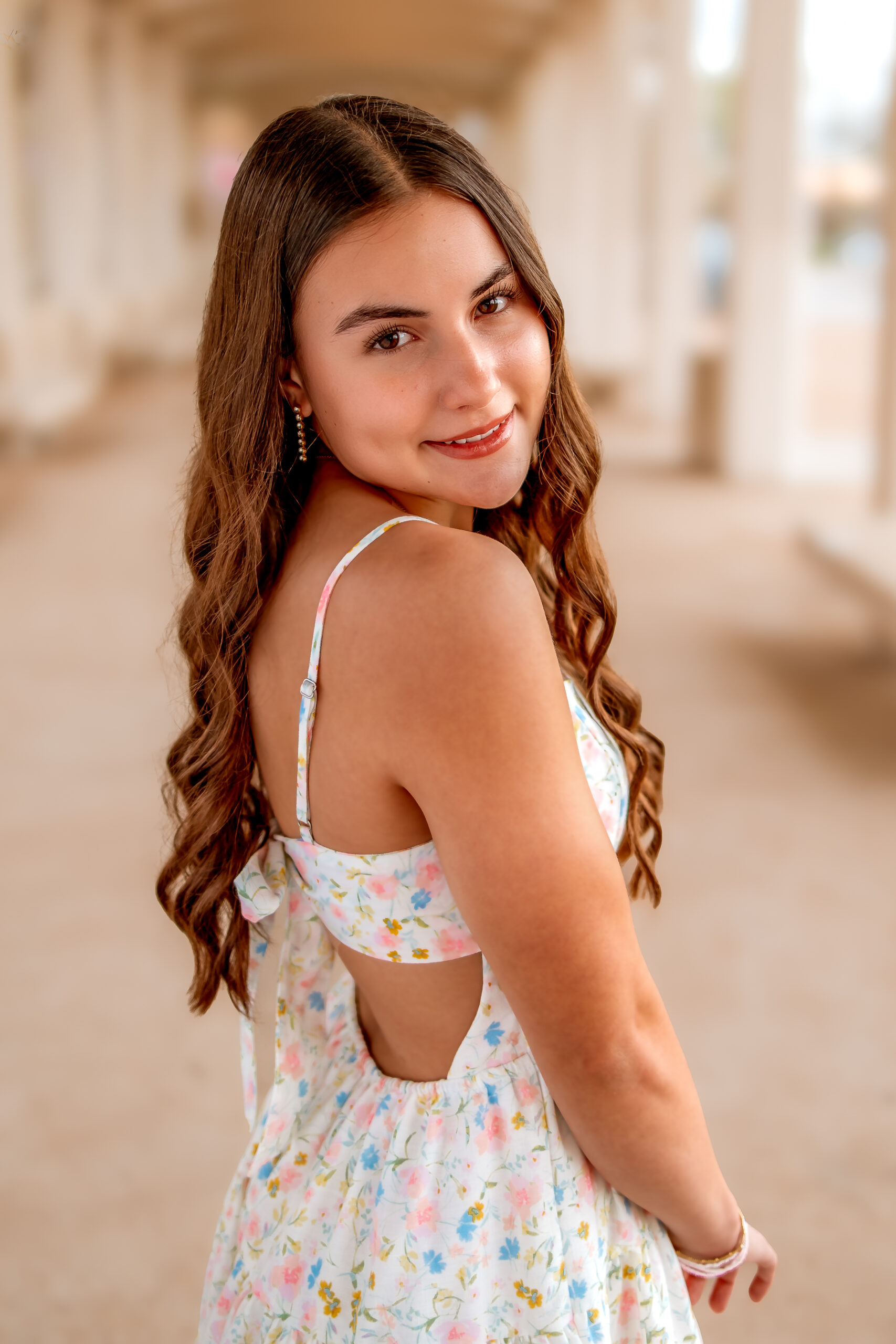 A beautiful young girl is looking over her right shoulder and softly smiling for her senior photos. 