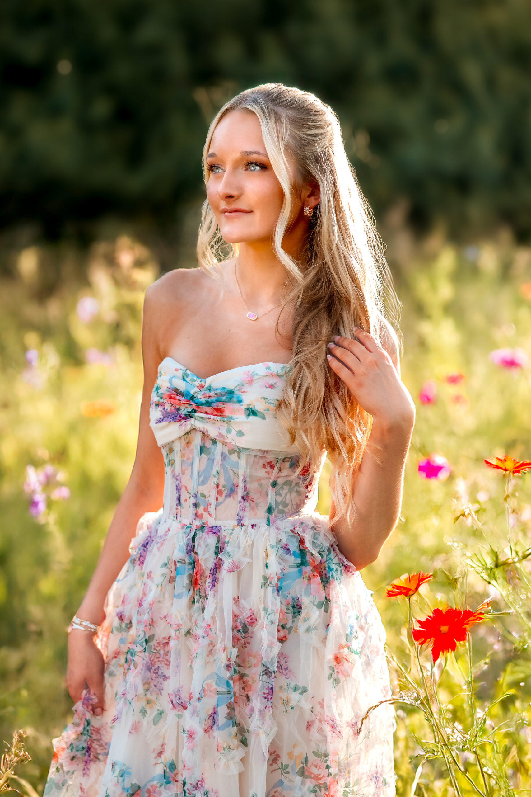 A lovely young senior girl in a field of wild flowers with a strong backlight of the summer glow of sunset behind her highlighting the field and the wild flowers.