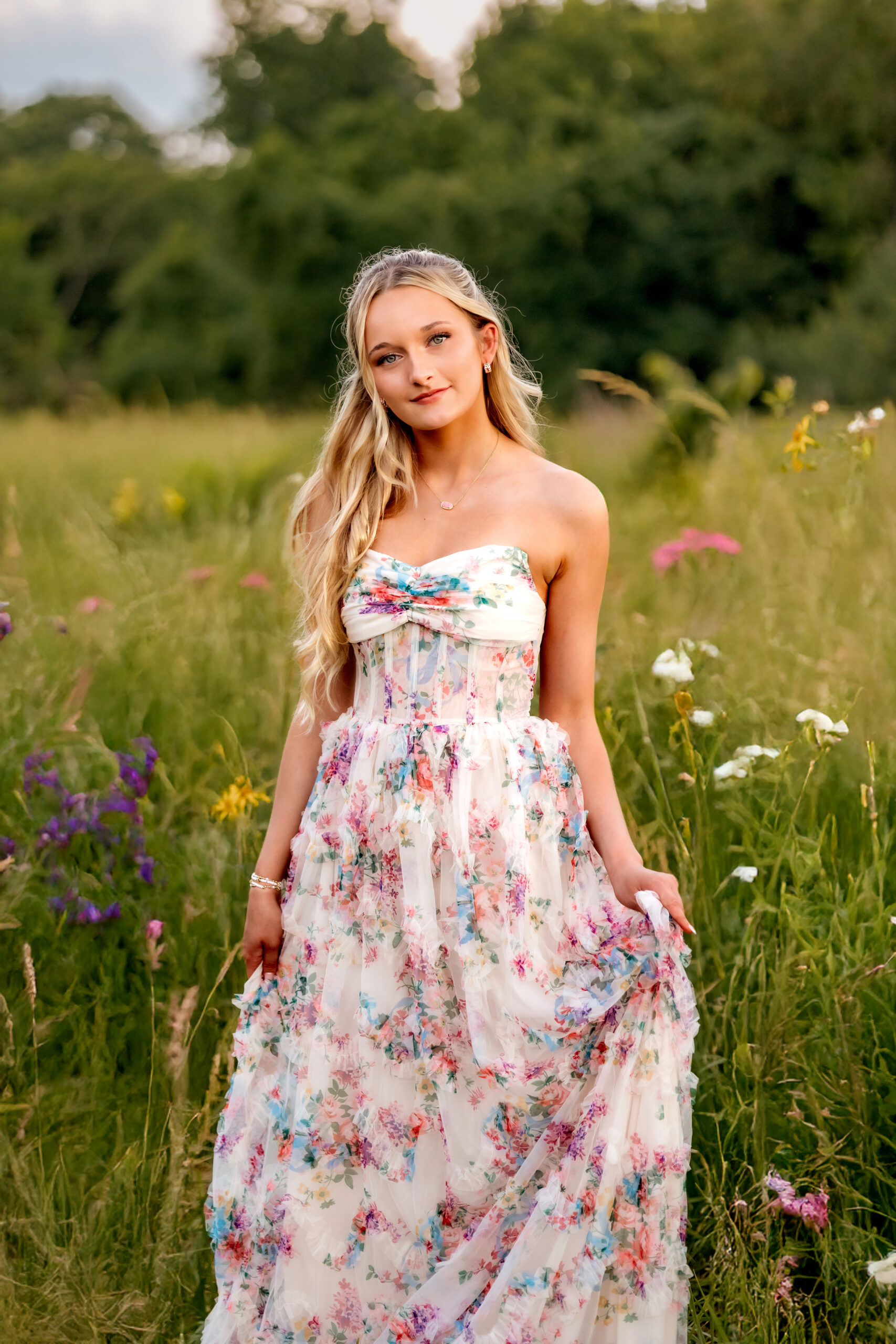 A lovely young senior girl in a field of wild flowers with a strong backlight of the summer glow of sunset behind her highlighting the field and the wild flowers.