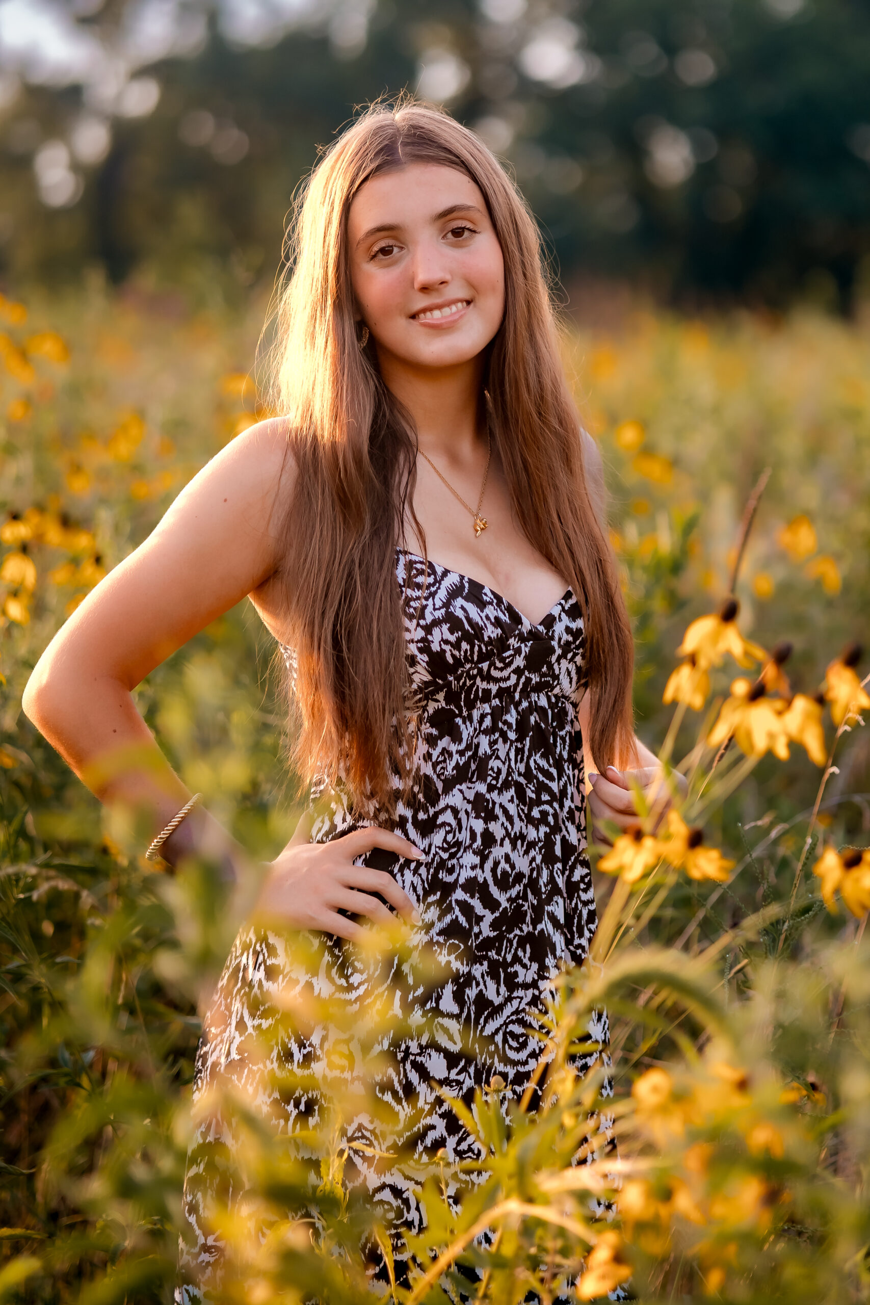 a girl is standing in a field with her long floral dress on and she is surrounded by wild flowers at sunset.