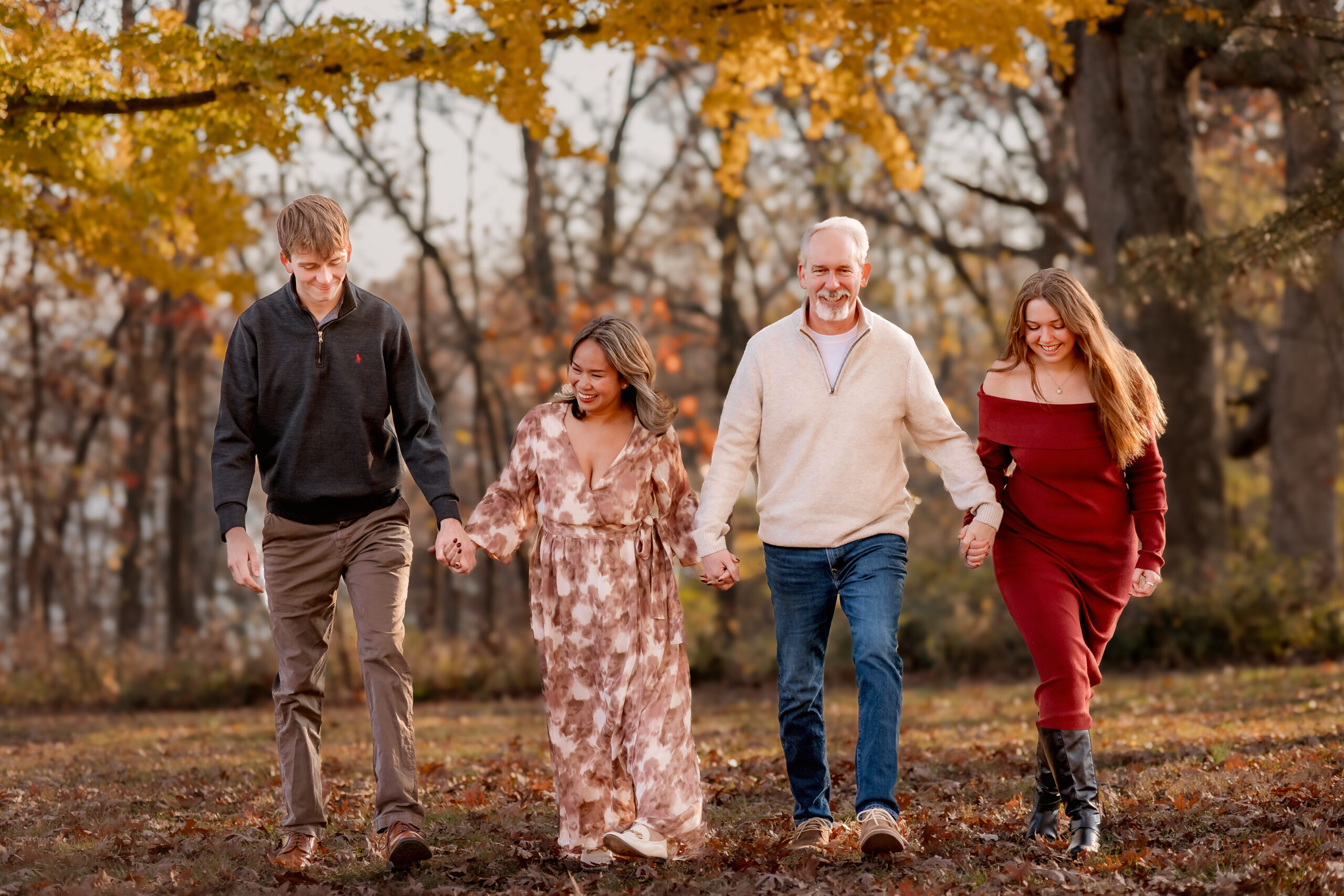 a family of four is walking together arm in arm laughing and looking at each other. The fall leaves have fallen and this is the best holiday family photography St. Louis.